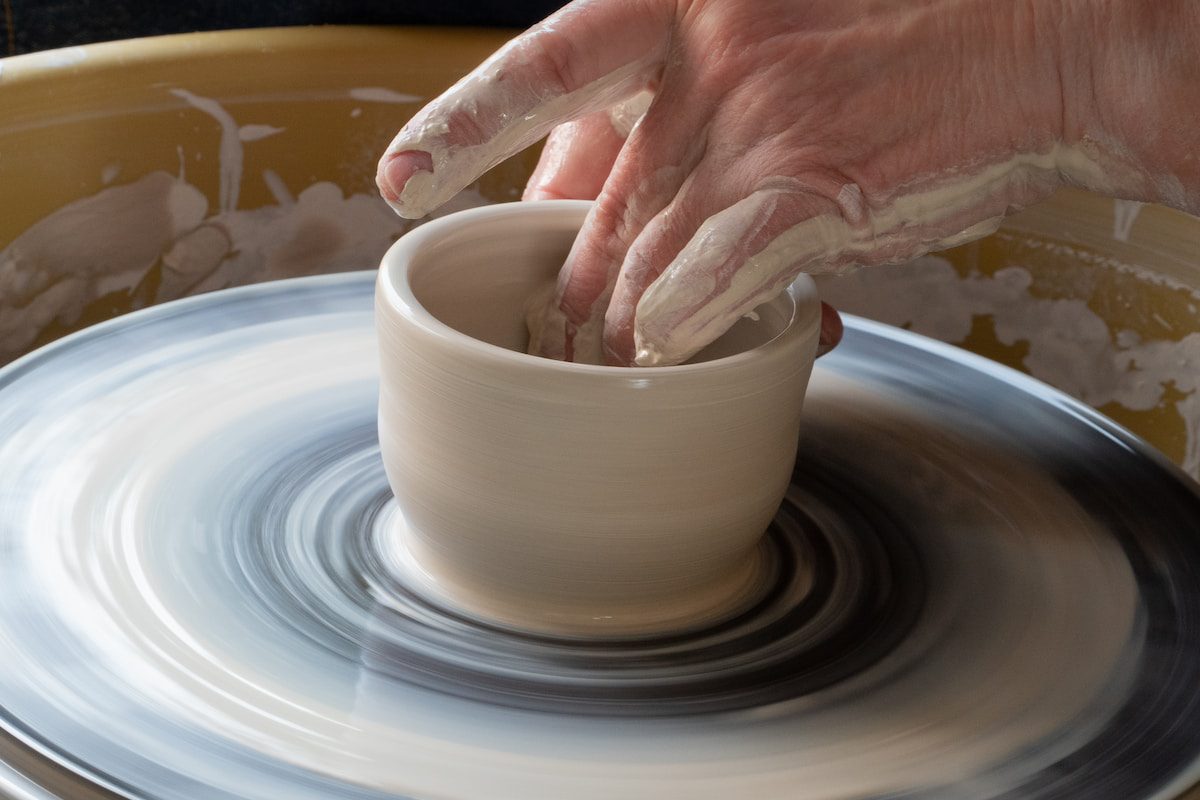 person making clay pot on white round plate - Handmade Pottery and Clay Goods